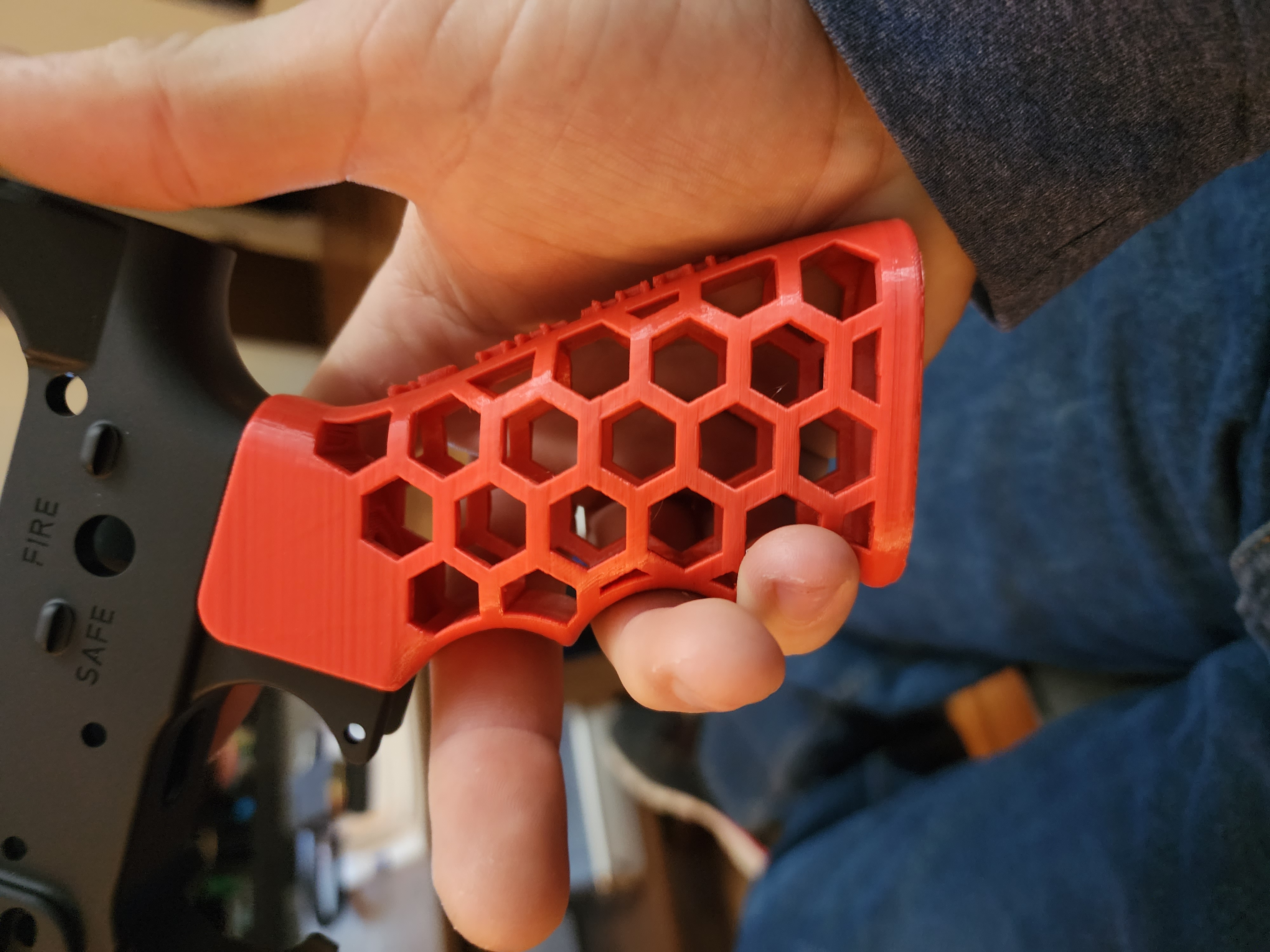Red 3D printed AR-style pistol grip with a hexagonal honeycomb lattice